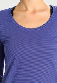 Lila långärmad tröja med tunna vita horisontella ränder, rund halsringning och mjukt, strukturerat tyg. Inga synliga logotyper eller mönster.