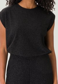 Top corto nero brillante con maniche corte e vestibilità rilassata, dotato di scollo rotondo, realizzato in tessuto testurizzato. Senza chiusure visibili o motivi.