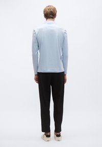 Ανοιχτό μπλε μακρυμάνικο πουκάμισο με γιακά, λεία υφή· συνδυασμένο με μαύρο παντελόνι και μπεζ παπούτσια με μαύρες λεπτομέρειες.