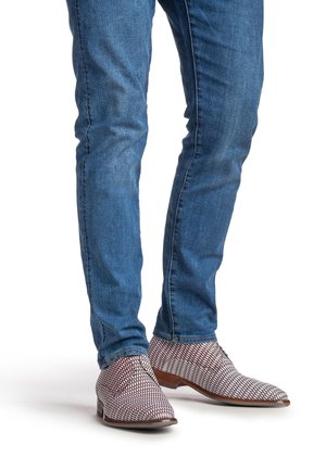 Chaussures en tissu rouge et blanc à motif, dotées d'un petit talon et d'un laçage, portées avec un jean bleu ajusté.