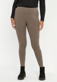 Bruine stretchleggings gemaakt van een gladde, zachte stof met een elastische taille, gecombineerd met zwarte enkellaarzen.