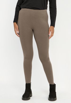 Bruine stretchleggings gemaakt van een gladde, zachte stof met een elastische taille, gecombineerd met zwarte enkellaarzen.