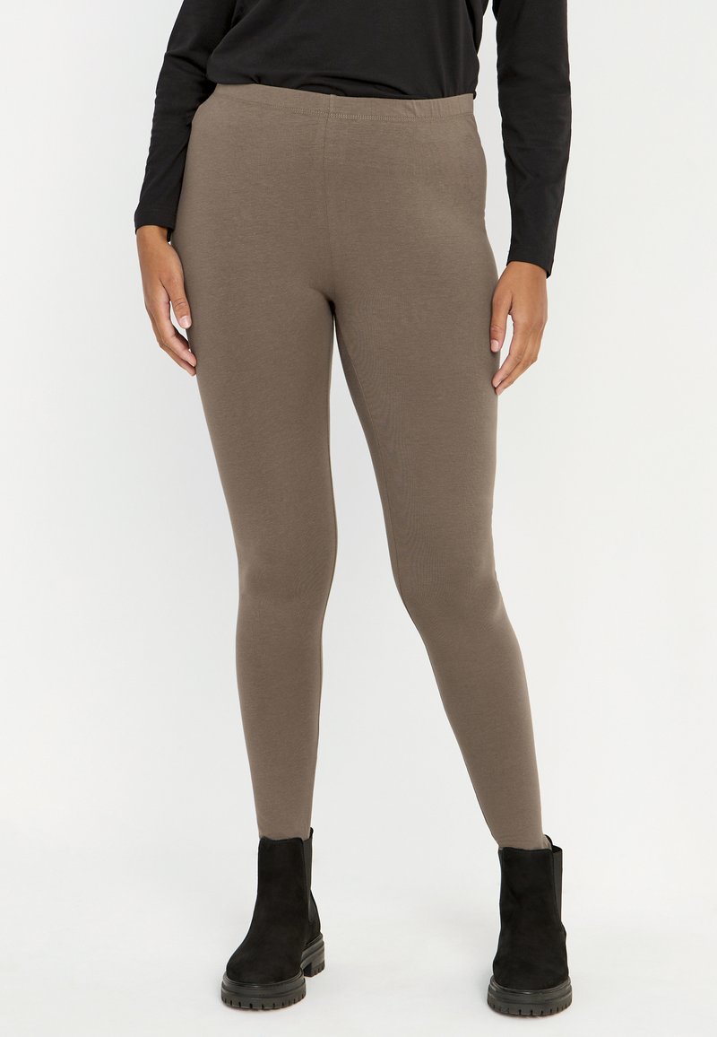 Bruine stretchleggings gemaakt van een gladde, zachte stof met een elastische taille, gecombineerd met zwarte enkellaarzen.