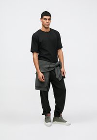 Černé tričko s krátkým rukávem, šedá mikina uvázaná kolem pasu, černé zúžené kalhoty a šedé vysoké tenisky s červeným detailem.