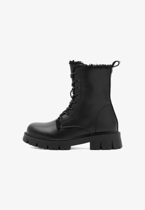 Fekete bőrbakancs texturált, műszőrme gallérral, fűzős előlappal és vastag gumitalppal, mély barázdákkal a tapadás érdekében.