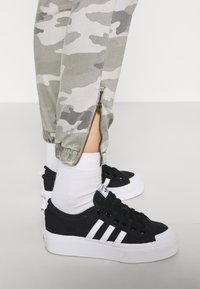 Svarta canvas sneakers med vita ränder, ihopparat med grå camouflage-joggers med sidoknäppning och elastiska mudd, bärs med vita strumpor.