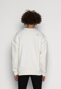 Ljus krämfärgad sweatshirt med avslappnad passform, rund halsringning och ribbade mudd. Har en liten, tonad logotyp på den övre delen av ryggen.