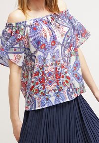 Blusa floreale senza spalle con motivi blu, rossi e verdi, maniche a volant e tessuto leggero e texturato.