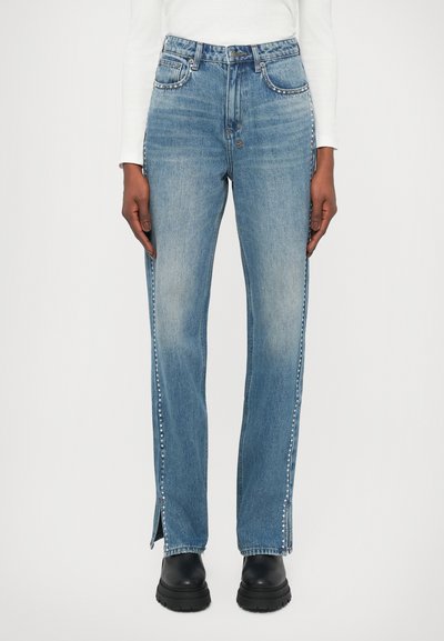 Jeans en denim bleu clair avec une coupe droite, dotés de fentes sur les côtés et de détails en clous métalliques le long des coutures. Design à cinq poches.