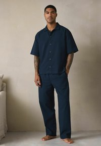 Sötétkék, rövid ujjú ing és nadrág szett textúrált anyagból, gombos előlappal és laza szabással, sima, diszkrét fényességgel.