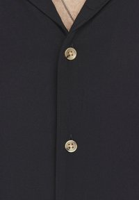 Camisa negra de botones con cuello, dos botones dorados y una tela suave y texturizada. Adecuada para ocasiones informales o formales.