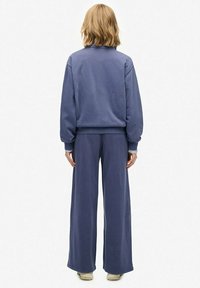 Sudadera azul de corte relajado y pantalones de pierna ancha en tejido suave. Cuenta con puños y dobladillo acanalados, diseño minimalista y sin patrones visibles.