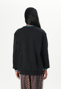 Sort sweatshirt med blå detaljer langs halsudskæringen og manchetterne, med en løs pasform og lange ærmer, parret med bukser i leopardmønster.