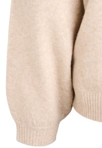 Bežs džemperis ar mīkstu, teksturētu apdari, ribotiem piedurkņu galiem un brīvu piegriezumu ar noliktām plecu daļām. Materiāls izskatās silts un ērts.