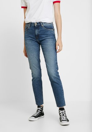 Jeans de talle alto de color azul oscuro con pierna recta, que presentan un dobladillo desgastado. Combinados con una camiseta blanca y zapatillas altas negras.