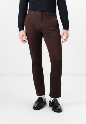 Bruine chino's met een gladde textuur, slim fit, zijzakken en een enkele knoopsluiting. Gecombineerd met zwarte instappers en grijze sokken.