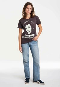 Black cotton T-shirt with a graphic print of a man’s face and the text "Just one more thing!" paired with light-wash straight-leg jeans.
