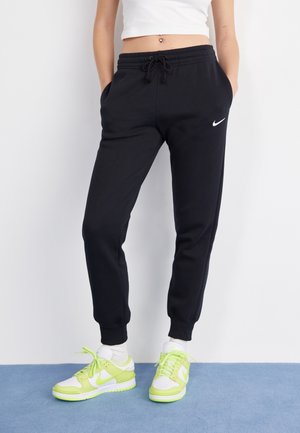 Black sweatpants with elastic waistband and cuffs, featuring a small white Nike logo. Paired with white and neon green Nike sneakers.