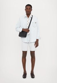 Giacca di jeans chiara sopra una camicia floreale, abbinata a pantaloni corti chiari. Borsa a tracolla nera, scarpe scure. Outfit semplice e casual.