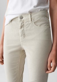 Beige corduroy broek met een aansluitende pasvorm, voorzien van een knoopsluiting, voorkruiszakken en een subtiele ribbeltextuur.
