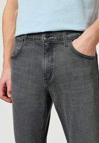 Jeans de mezclilla gris con un ligero desgaste, cinco bolsillos y cierre de botón metálico. La tela presenta una textura suave con sutiles detalles de costura.