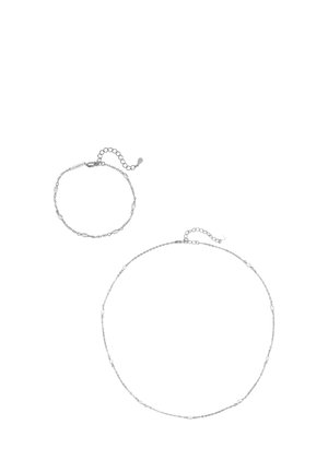 Zarter silberner Kettenarmband und passende Halskette mit kleinen ovalen Perlen und verstellbaren Verschlüssen auf weißem Hintergrund.