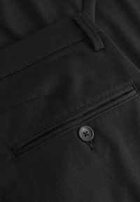 Schwarze Hose aus glattem Stoff, ausgestattet mit einer flachen Tasche mit horizontalem Öffnungsdesign und einem schwarzen Knopfdetail.