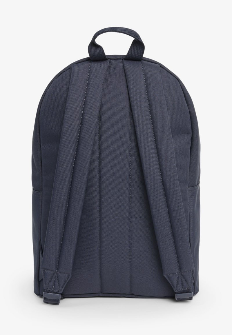 Zaino blu scuro visto da dietro con spallacci imbottiti e una maniglia superiore per il trasporto su sfondo bianco.