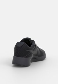 Svart Nike träningsskor med mesh-tyg, dämpad sula och Nike-logotyp, visad från en bakre vinkel på vit bakgrund.