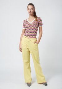 Top de manga corta y escote en V en un patrón de zigzag rosa y amarillo, combinado con pantalones de pierna ancha amarillos con bolsillos laterales y cordón.