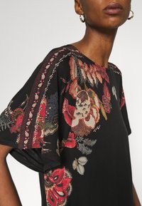 Svart kortärmad blus med intrikata blommönster i röda, vita och blå nyanser, med en mjuk, strukturerad yta och rund halsringning.