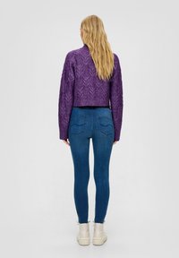 Fioletowy sweter typu cropped z dzianiny o splocie, w połączeniu z ciemnoniebieskimi spodniami skinny z wysokim stanem i białymi botkami za kostkę.