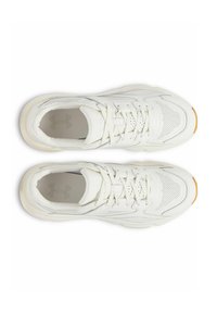 Baskets de sport blanches avec une tige texturée, des détails perforés, des lacets plats et une semelle en caoutchouc comportant une subtile touche orange au niveau des orteils.