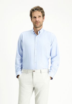 Camisa de botones de manga larga de color azul claro con cuello, hecha de material suave. Metida en unos pantalones de color claro, con botones visibles.