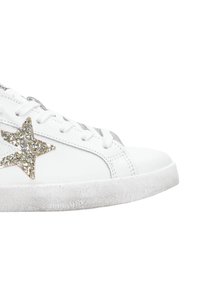 Sneaker bianco in pelle con suola in gomma texture, dotata di una grande stella dorata glitterata sul lato e dettagli argentati sui lacci.