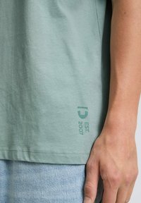 Miętowa koszulka z krótkim rękawem, wykonana z bawełny, z małym logo "EST 2007" w kontrastowym odcieniu w pobliżu dołu.