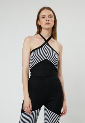Top de halter blanco y negro con un patrón de rayas que transiciona a negro sólido; hecho de una tela elástica. Combinado con leggings negros.