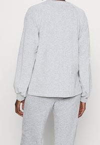 Sudadera gris con mangas largas y abullonadas y un ajuste holgado. Textura suave, escote redondeado y el dobladillo cae justo por encima de la cintura.