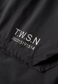 Schwarzer Stoff mit weiß gedrucktem Text "T.W.S.N" über einer 10-stelligen Zahl "202315191514" auf einem gefalteten Abschnitt des Materials.