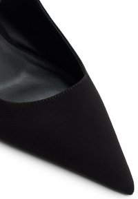 Zapato negro de punta afilada con una textura de ante suave y un diseño de lado abierto. El interior presenta un acabado mate suave.