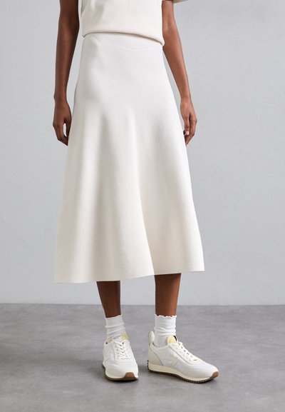 Jupe A-line blanche, longueur genou, en tissu texturé, associée à des baskets blanches et des chaussettes blanches côtelées. Design doux et minimaliste.