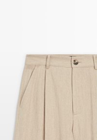 Beige hoge taille broek met riemlussen, zijzakken, plooien en een enkele knoopsluiting op de tailleband.