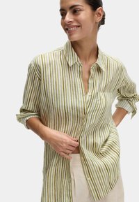 Camicia di lino a righe verde e bianca con maniche lunghe, chiusura a bottoni, colletto e tasca sul petto. Tessuto leggero e strutturato.