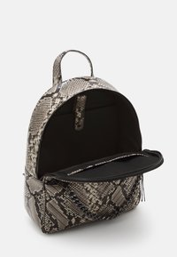 Sac à dos avec un motif imitation peau de serpent en gris et noir. Forme arrondie, fermeture éclair, poche intérieure, poignée supérieure et détail accentu é en chaîne.