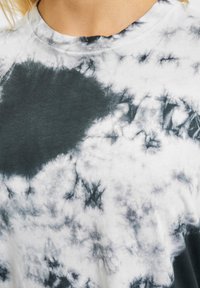 Bomullströja med ett svart och vitt tie-dye-mönster, rund halsringning och en mjuk, texturerad yta med varierande nyanser och stänk.
