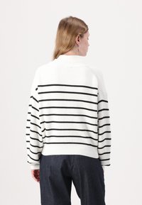 Strikket genser i hvit med svarte horisontale striper, med rund hals og ribbestrikkede mansjetter. Myk tekstur, avslappet passform.