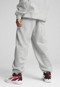 Grå sweatpants lavet af blødt stof, med en afslappet pasform og elastiske manchetter, parret med sorte og røde sporty sneakers.