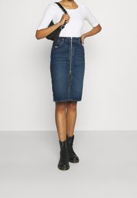 Blå denimpennkjol med dragkedja fram, knälång, kombinerad med en vit åtsittande topp och svarta snörade kängor. Minimalistisk design.