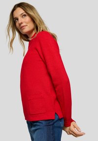 Roter Strickpullover mit rundem Ausschnitt, langen Ärmeln und einer Fronttasche. Verfügt über seitliche Schlitze und eine strukturierte Oberfläche.