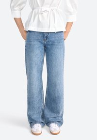 Jeans a gamba larga di colore azzurro chiaro realizzati in denim, con vita alta, un classico design a cinque tasche e bordi sfrangiati.